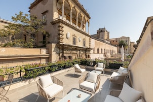 A rooftop terrace with wicker furniture and a view of historic buildings.