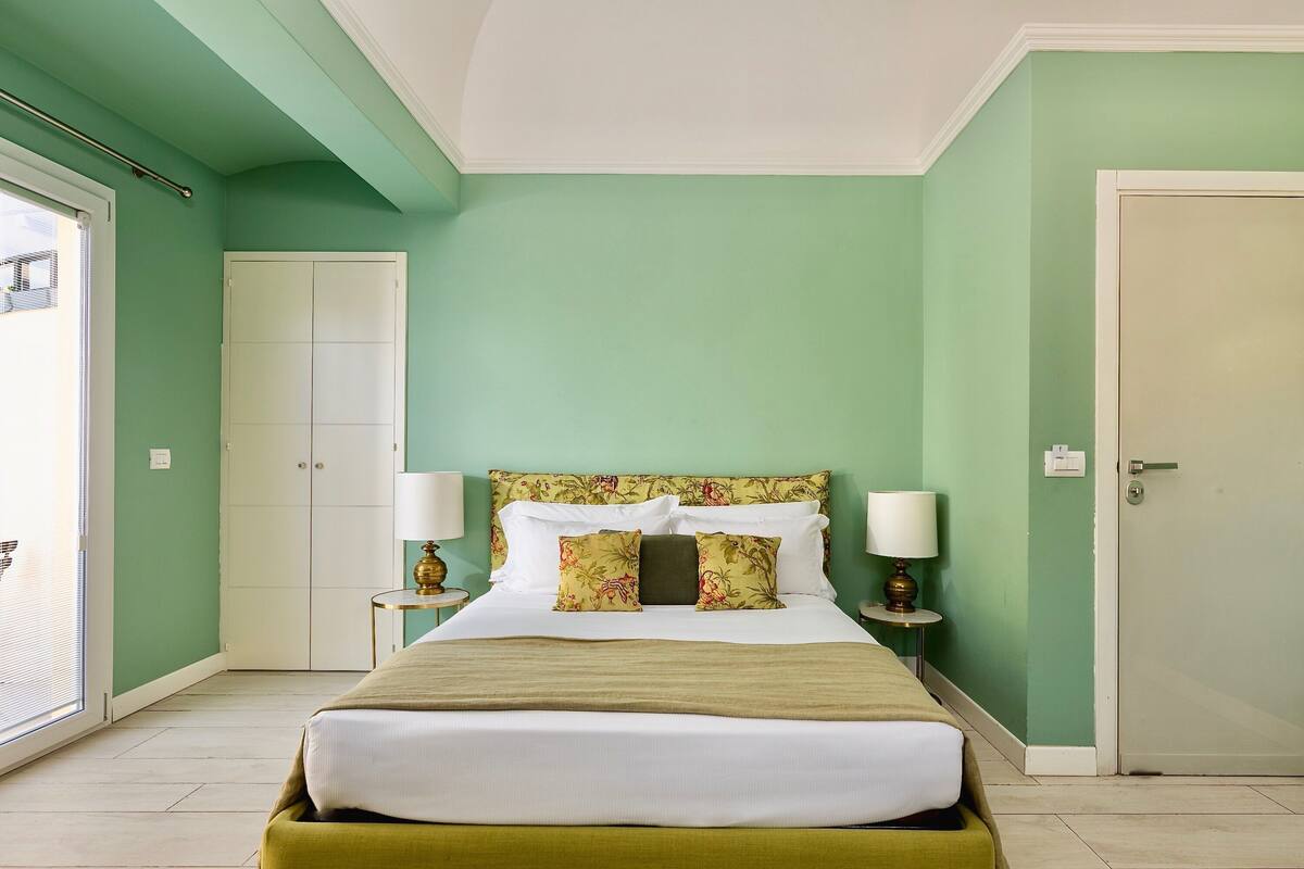 Une chambre à coucher bien rangée, avec un lit, deux tables de chevet, une fenêtre et une porte.