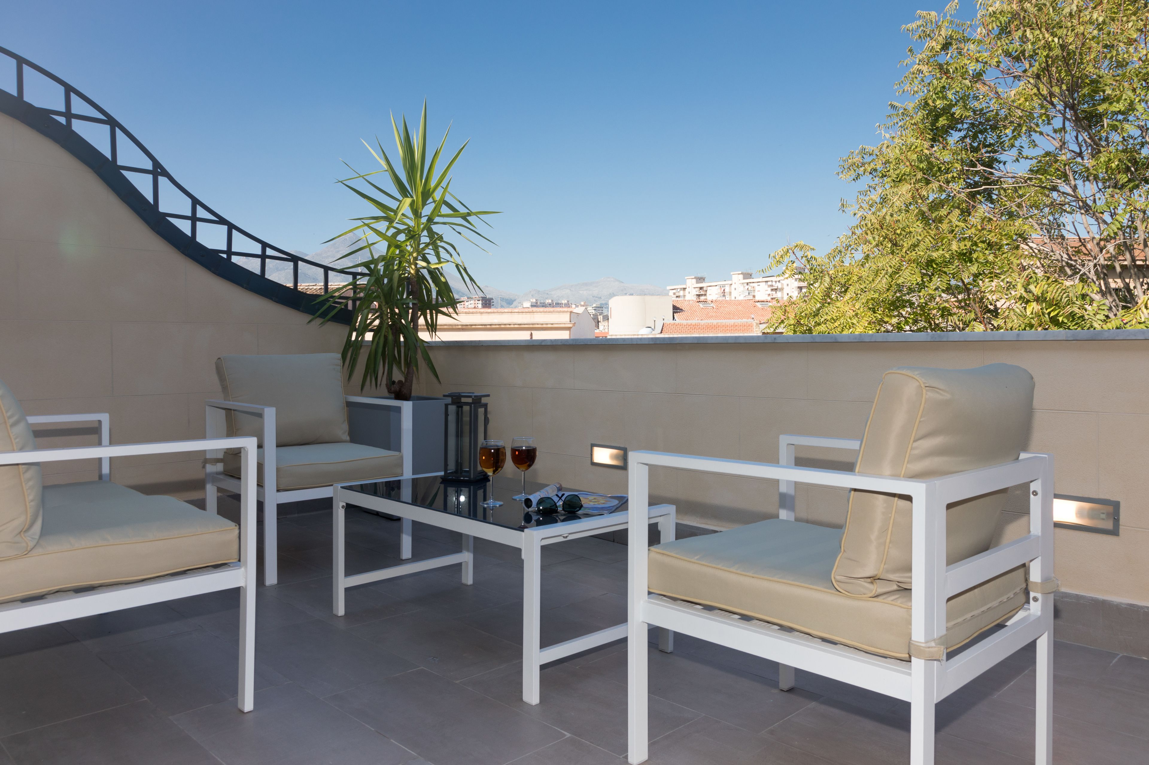 Terraza en la azotea con mobiliario blanco, una mesa de vidrio y una planta en maceta.