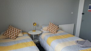 A hotel room with two beds, patterned bedding, a small round table with a lamp, and a radiator. - Marlborough Hotel (Hull)