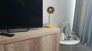 A wooden cabinet with a television and remote control, a small table with a white pitcher and a glass, and a patterned wall. - Marlborough Hotel (Hull)