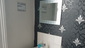 A bathroom with a white sink, a mirror, a trash bin, and a chair. - Marlborough Hotel (Hull)