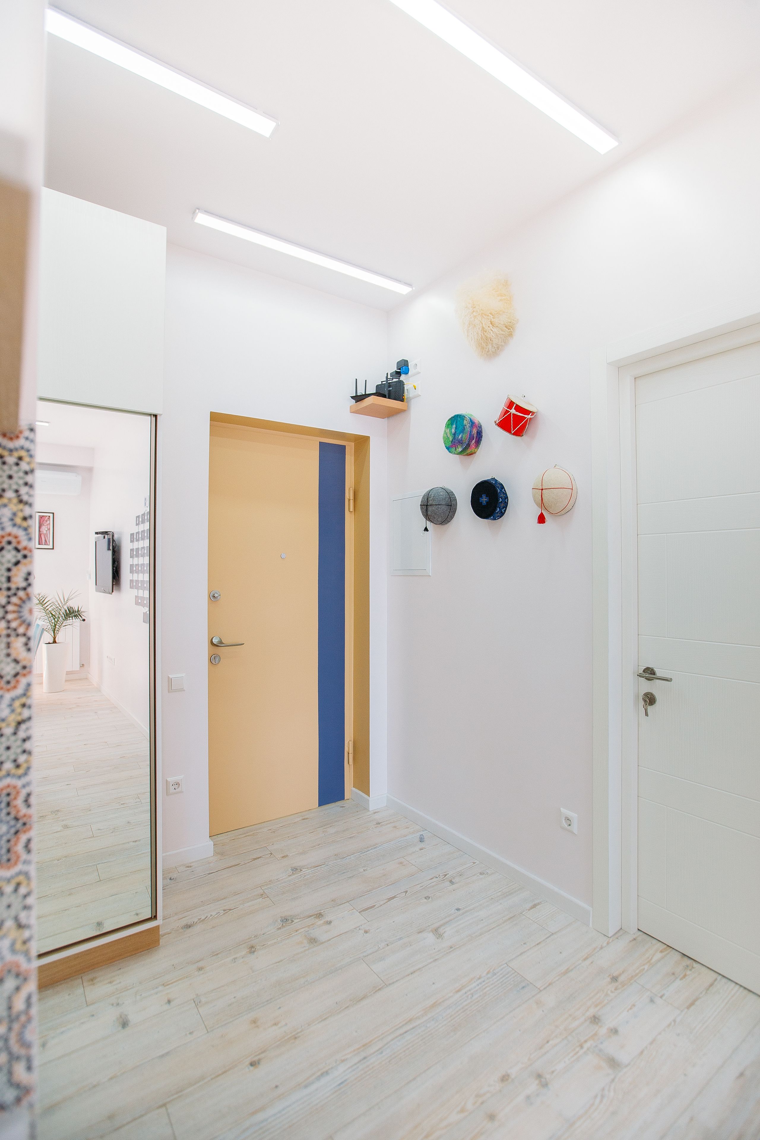 A hallway with a wooden door, a blue vertical stripe, and a wall with various hats.