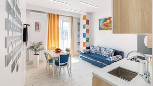 Een moderne keuken met een spoelbak, eettafel en stoelen. Er staat een blauwe bank met gekleurde kussens en er hangt een schilderij aan de muur.