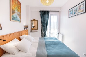 A neatly made bed with white and teal bedding, a wooden headboard, and a large window with a view of trees.