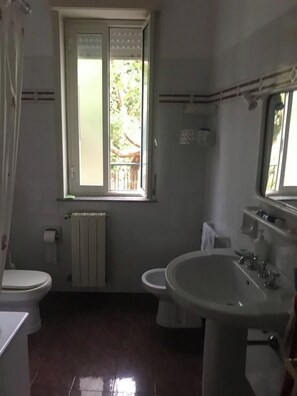 A bathroom with a toilet, bidet, sink, and a window. - Villa Gallo Antony (Patti)