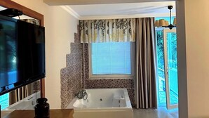 A modern bathroom with a bathtub, a shower, and a toilet. There is a television on a wooden stand and a bottle of water on the counter. - Sweet Home River Hotel (Sile)