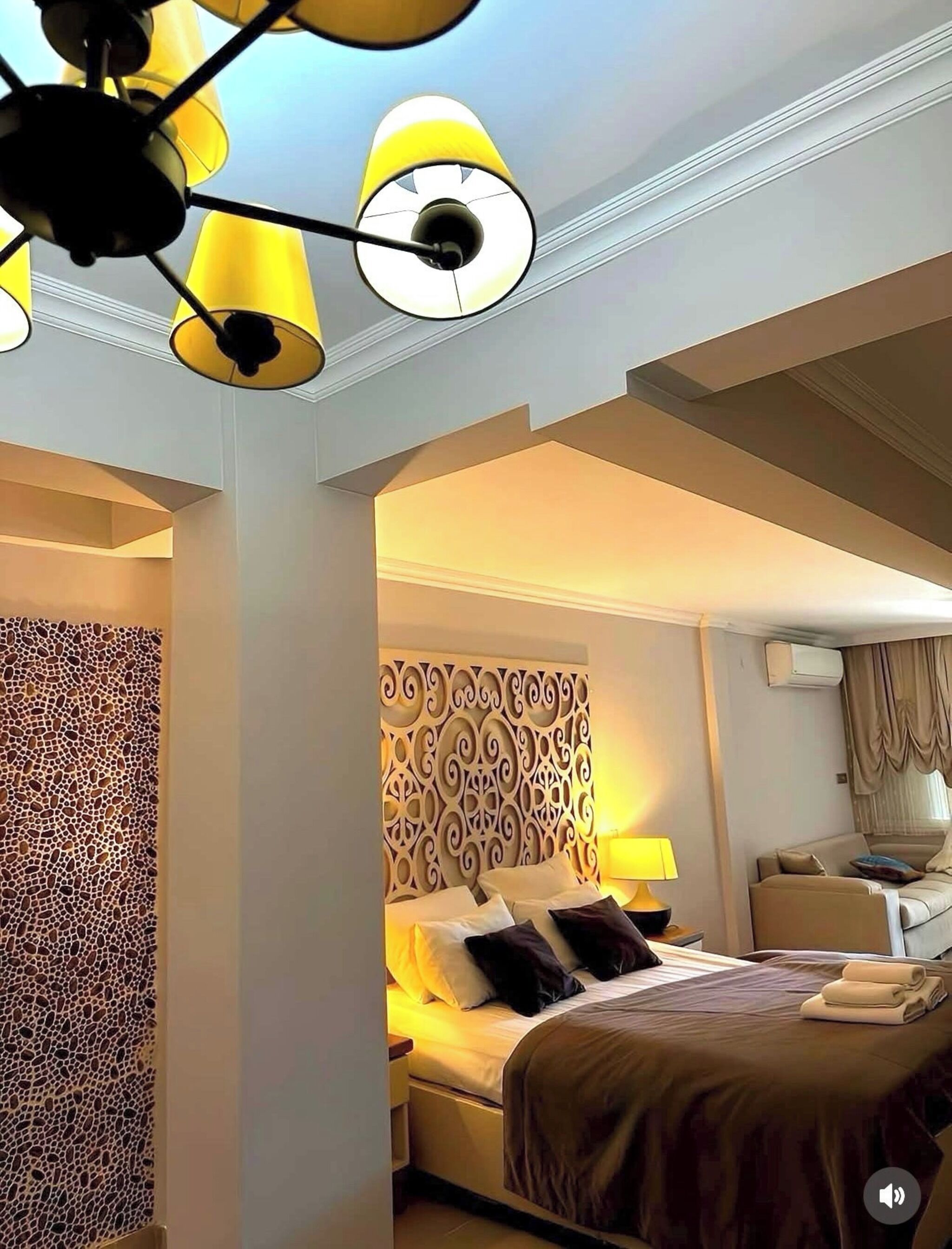 Een hotelkamer met een bed, een decoratief hoofdbord, een nachtkastje, een lamp en een plafondlamp.