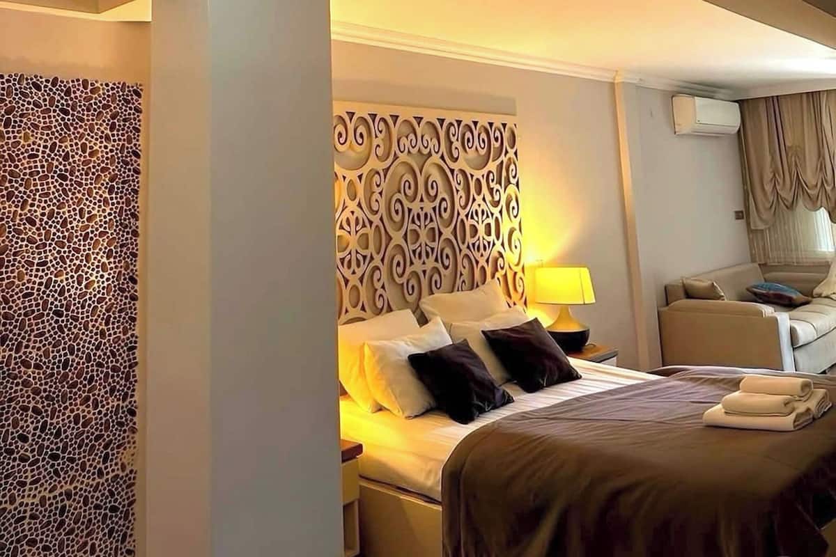 Habitació d'hotel amb un llit, un panell decoratiu al capçal, una taula de nit, una làmpada i una lluminària al sostre.