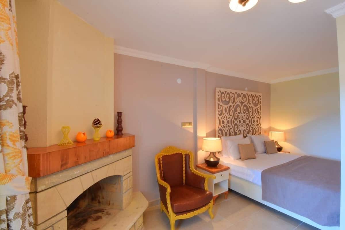 Habitació d'hotel amb una llar de foc, un llit, una taula de nit amb làmpades i un panell decoratiu a la paret.