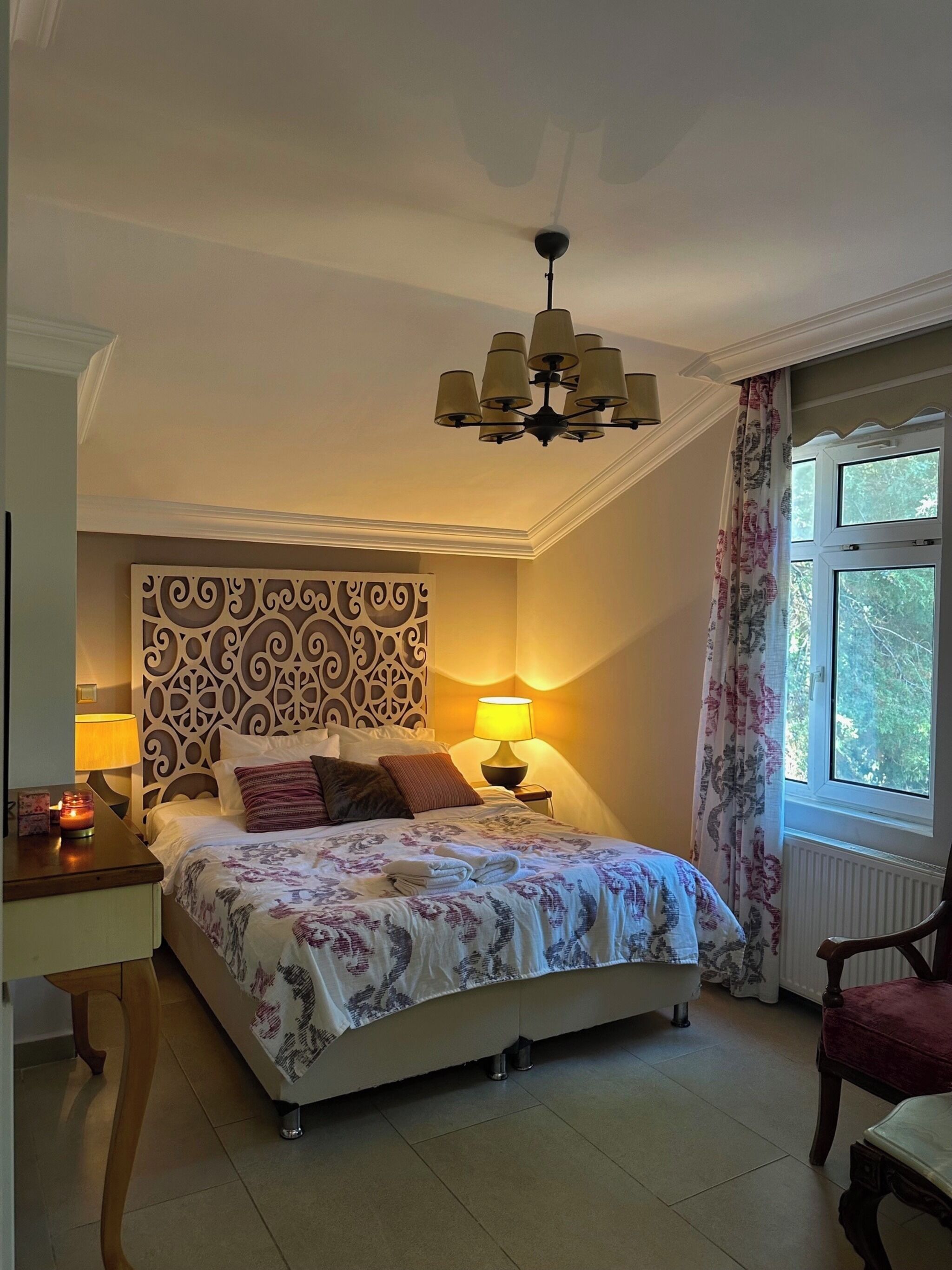 Een slaapkamer met een bed, nachtkastje, lamp en een raam met gordijnen.