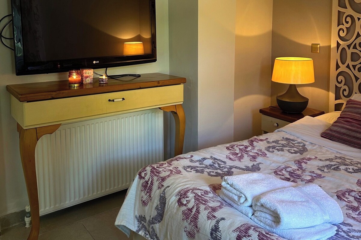 A hotel room with a bed, a TV on a wooden dresser, a bedside lamp, and a radiator.