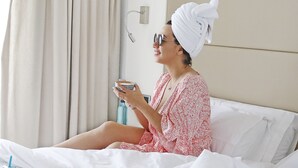 A person sitting on a bed with a tray of food, a drink, and a straw.