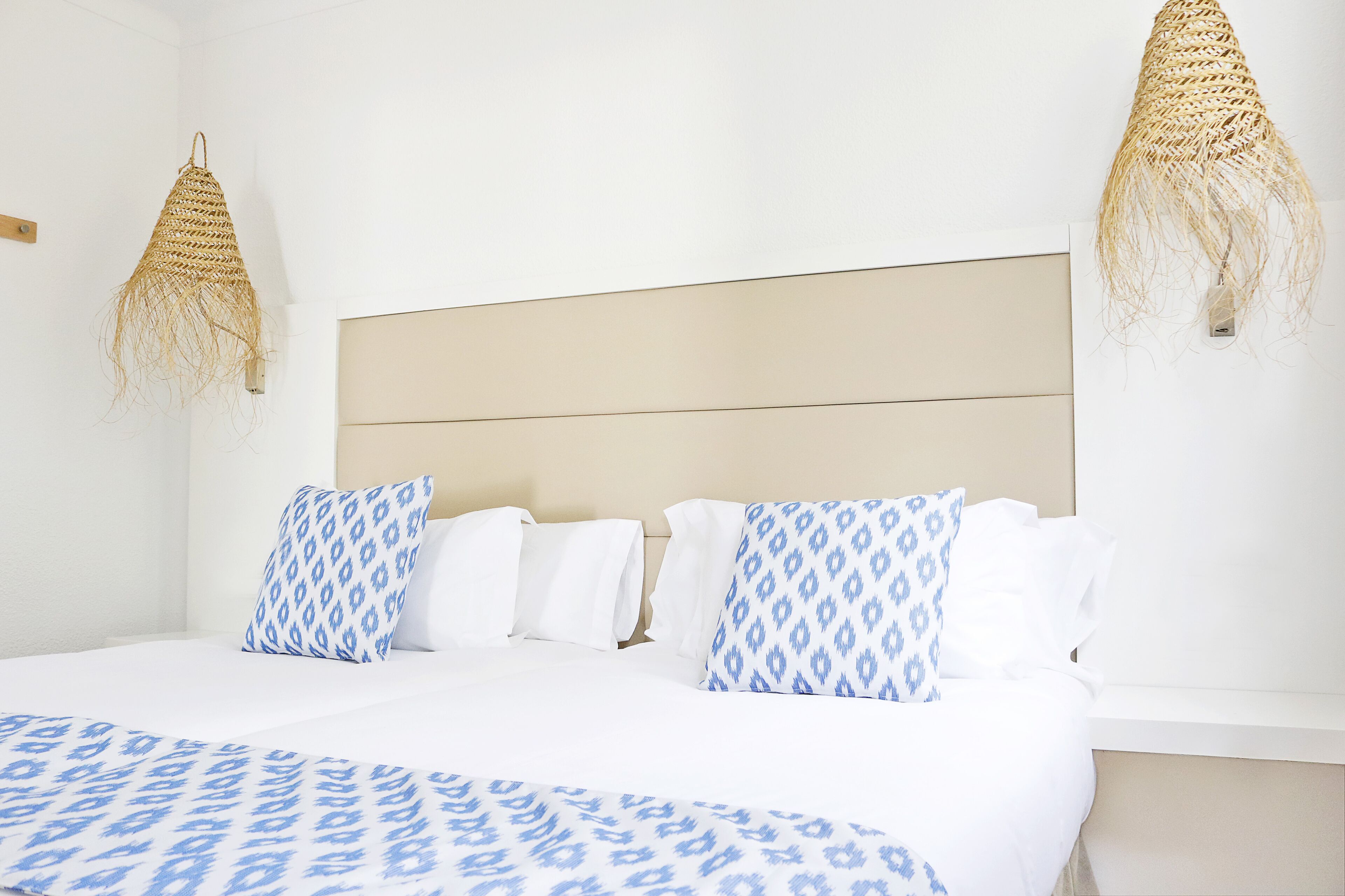Habitación de hotel con cama, ropa de cama blanca y azul estampada, y dos tapices tejidos.
