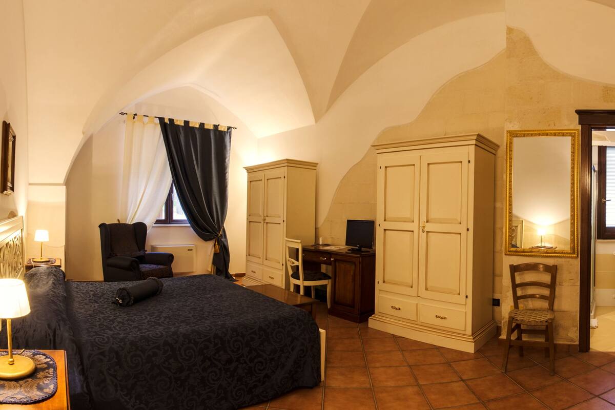 Une chambre avec deux lits, un bureau, une chaise, une armoire, un miroir et une salle de bain visible à travers une porte ouverte.