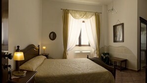 Ein Hotelzimmer mit Bett, Nachttisch, Lampe und einem Fenster mit Vorhängen.