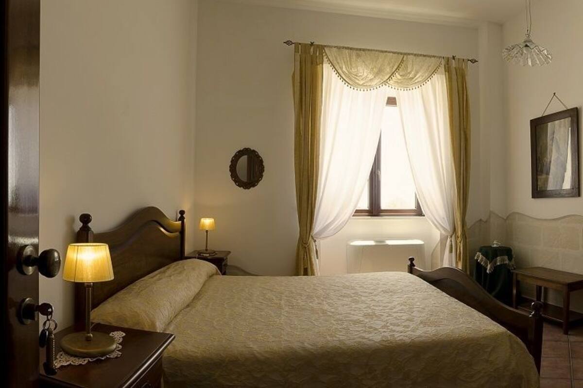 Une chambre d’hôtel avec un lit, une table de chevet, une lampe et une fenêtre avec des rideaux.