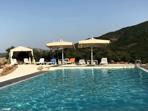 Une piscine entourée de chaises longues et de parasols, le tout niché dans un paysage vallonné.