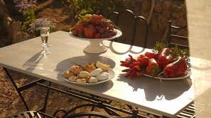 Une table dressée à l’extérieur, avec un plateau de fruits, une assiette de pâtisseries et un verre d’eau.