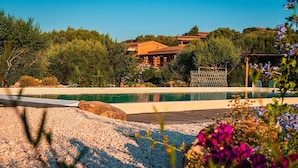 A pool with a wooden deck, surrounded by pebbles and plants.