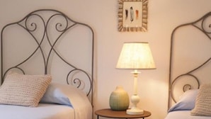 A double room with two beds, a small table with a lamp, and a wall-mounted picture.