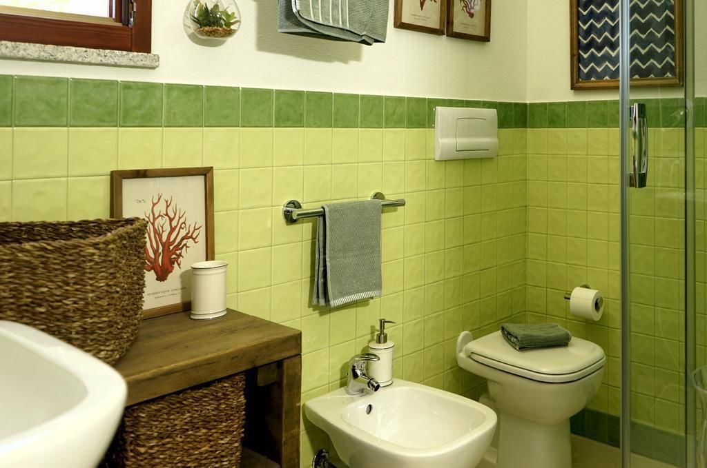 A bathroom with a green tiled wall, a white sink, a bidet, a toilet, and a shower area.