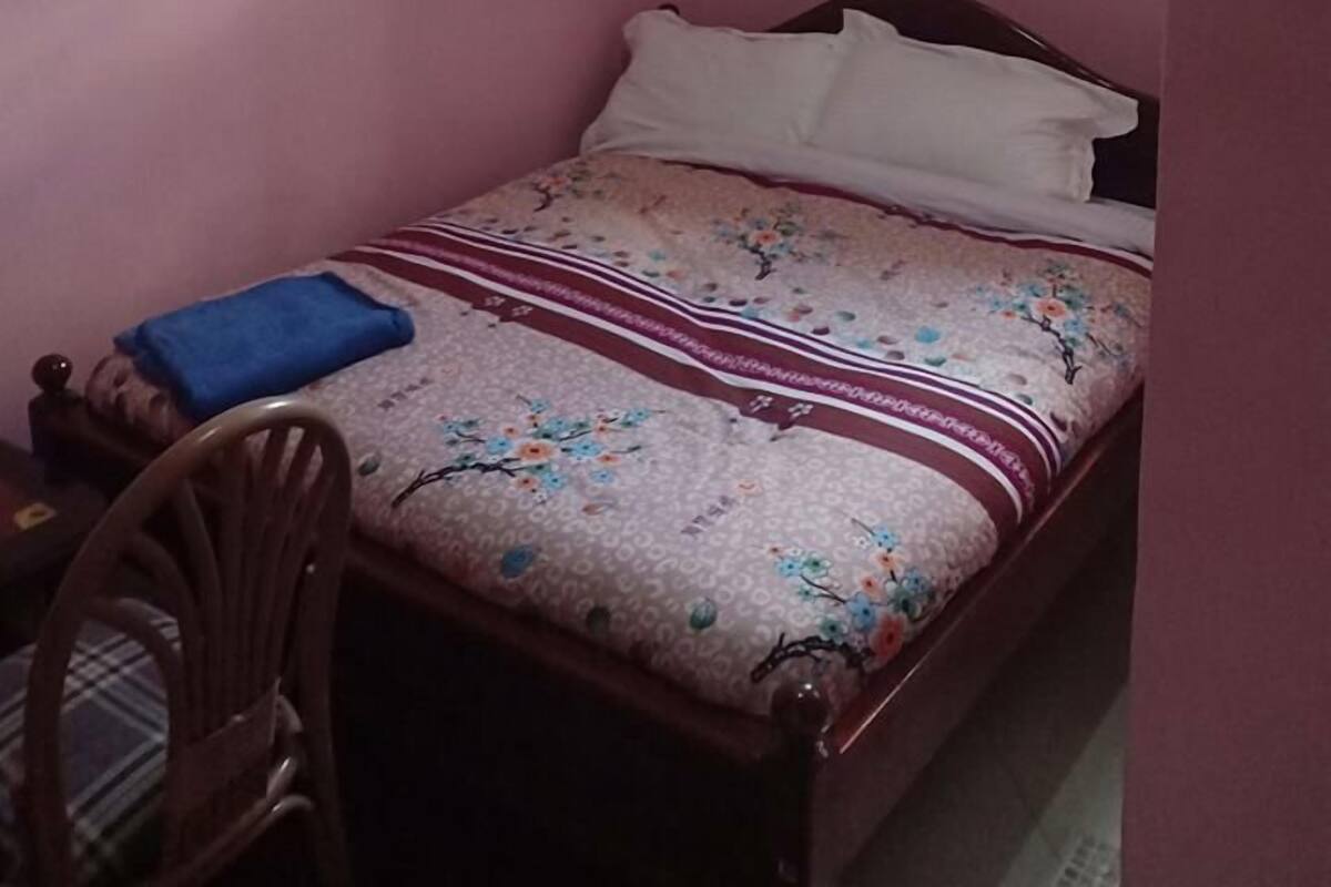 A small, pink-walled room with a single bed, a chair, and a window with curtains.