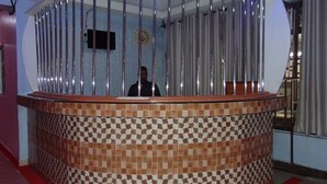 A reception area with a checkered tile floor, a wooden reception desk, and a person standing behind a metal barrier.