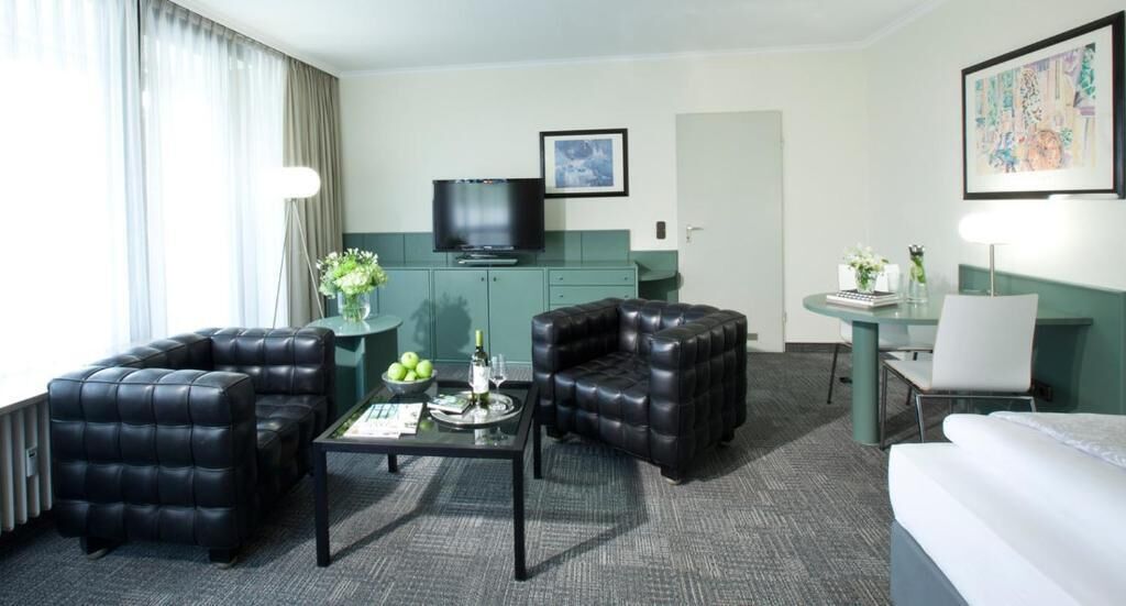 A hotel room with a seating area featuring two black leather sofas, a small coffee table, and a TV on a green cabinet.