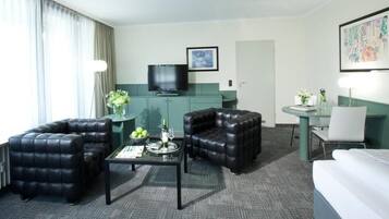 A hotel room with a seating area featuring two black leather sofas, a small coffee table, and a TV on a green cabinet.