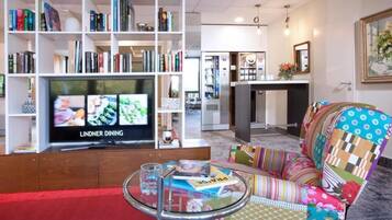 Ein modernes Wohnzimmer mit Flachbildfernseher, Bücherregal, farbenfroher Couch und kleinem Couchtisch.