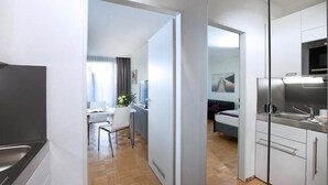 Une cuisine moderne équipée d’un four et d’un micro-ondes encastrés, un coin repas avec une table et des chaises, et une chambre avec un lit et une télévision.