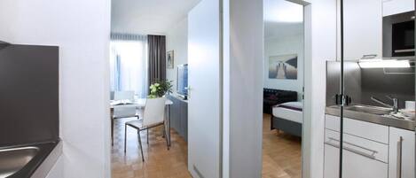 Una cocina moderna con horno y microondas integrados, un comedor con mesa y sillas, y un dormitorio con cama y televisor.