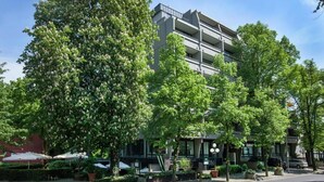 Un immeuble à plusieurs étages doté de balcons, entouré d’arbres verdoyants et sous un ciel dégagé.
