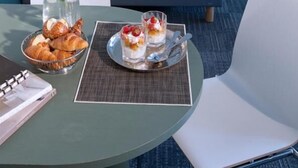 Une chambre d’hôtel avec un lit parfaitement fait, une table à manger avec des croissants et un dessert, et une lampe de chevet.