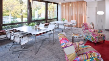 Une salle de conférence avec une grande table, des chaises blanches et des fauteuils aux couleurs vives.