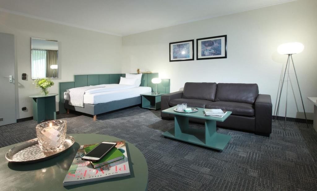 A hotel room with a bed, a sofa, a coffee table, a side table, a lamp, and a framed picture on the wall.
