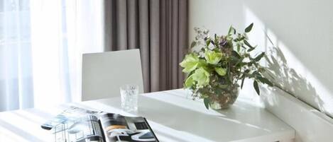 Un comedor moderno con una mesa blanca, una revista, un vaso de agua y una planta en maceta.