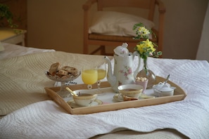 Een ontbijfwagen met thee, toast, sinaasappelsap en een bloevas op een bed.