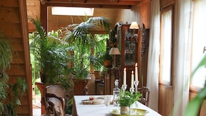 A wooden dining room with a table set for four, surrounded by chairs, and a chandelier above. - Chambres d’hôtes Au Jardin (Biscarrosse)