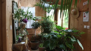 A wooden interior with potted plants, a statue, and a straw hat on the wall. - Chambres d’hôtes Au Jardin (Biscarrosse)