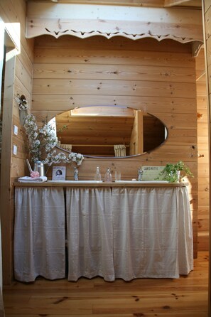 Een houten badkamer met een houten wastafel, een spiegel en een bordje met de tekst 'JARDINIERIE'.
