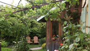 A wooden cabin with a garden patio, a table set for tea, and two wooden chairs. - Chambres d’hôtes Au Jardin (Biscarrosse)