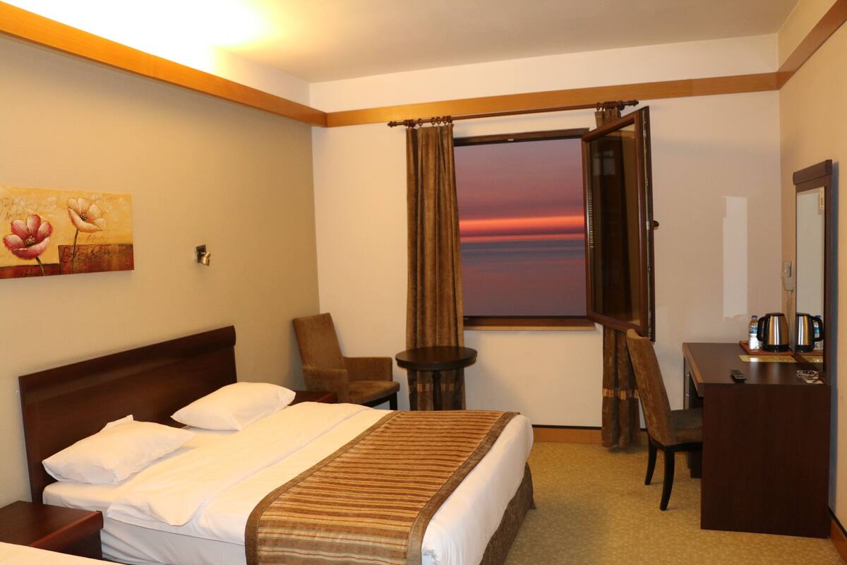 A hotel room with a large bed, a desk, a chair, a small table, and a window with curtains.
