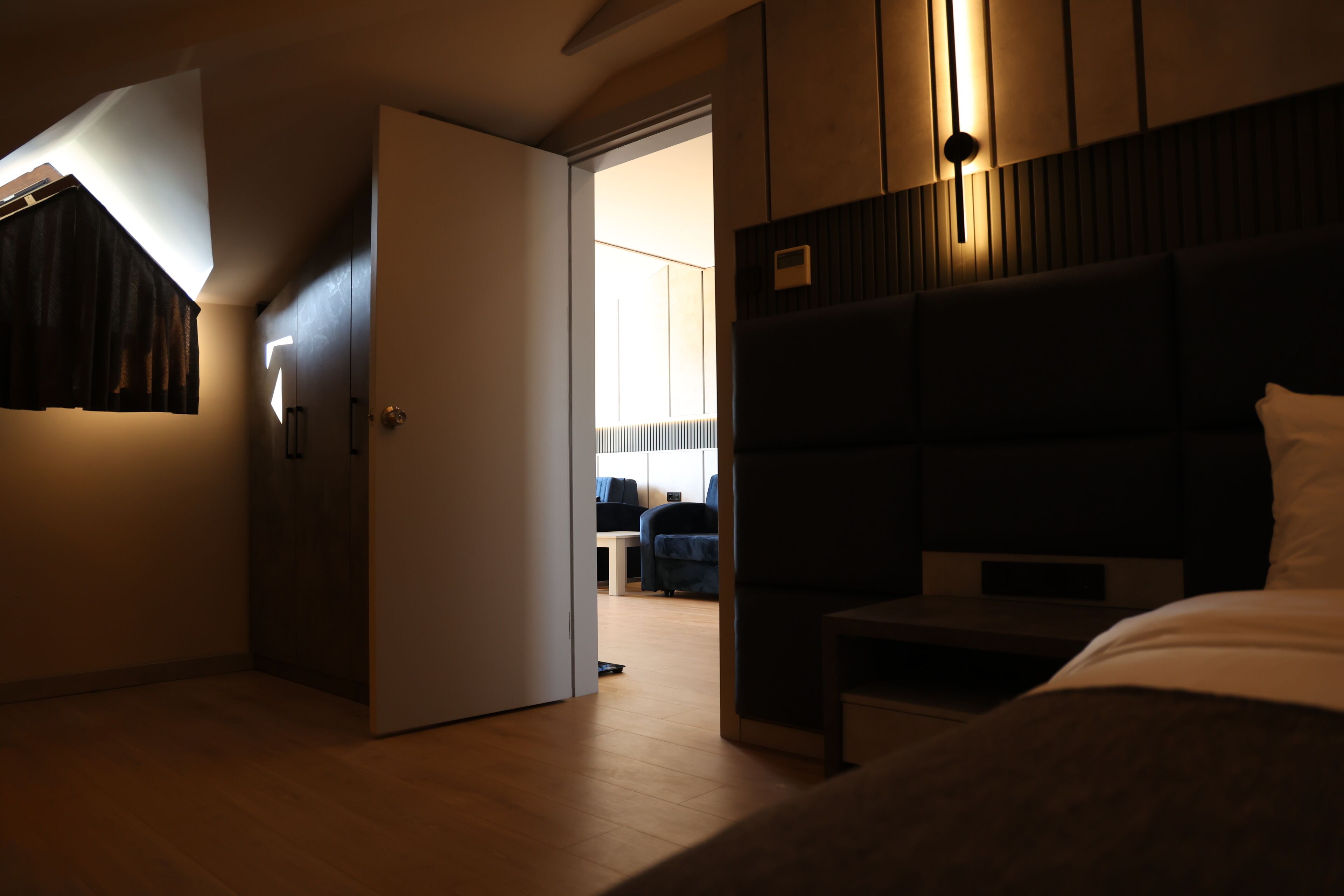 A hotel room with a bed, a desk, and a view of another room.