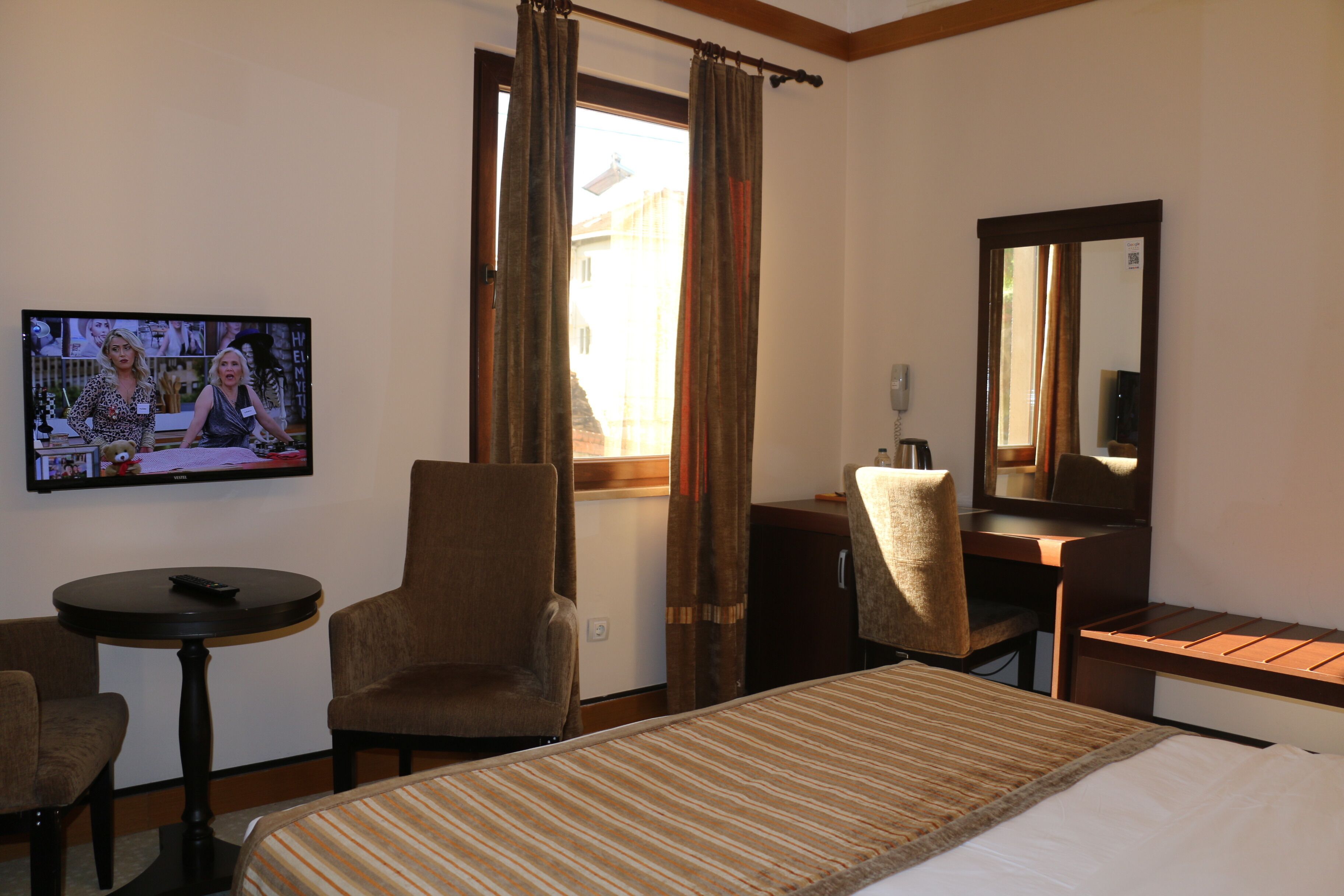 A hotel room with a bed, a desk, a chair, a television, and a window with curtains.