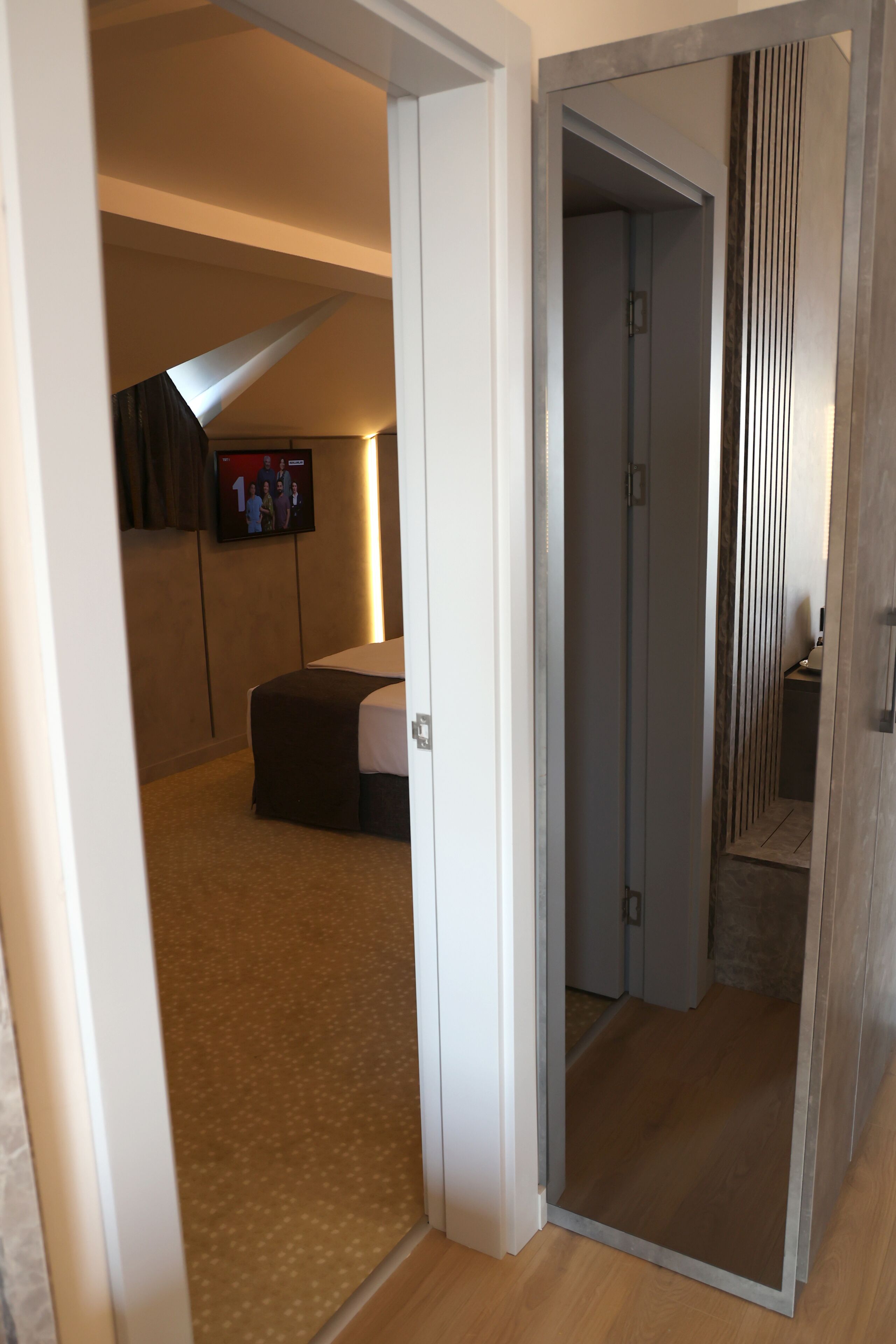 Habitació d'hotel amb un llit, una televisió penjada a la paret i un terra de fusta.