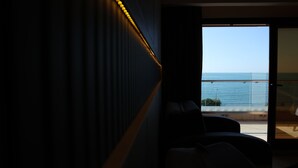 A room with a view of the sea through a large window, a dark wall with a light strip, and a seating area with a chair and a sofa. - Hotel Lazlakar (Çayeli)