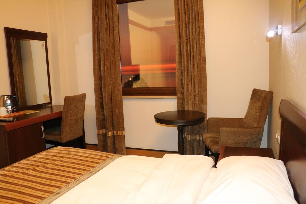 A hotel room with a bed, a desk, two chairs, a round table, and a mirror.