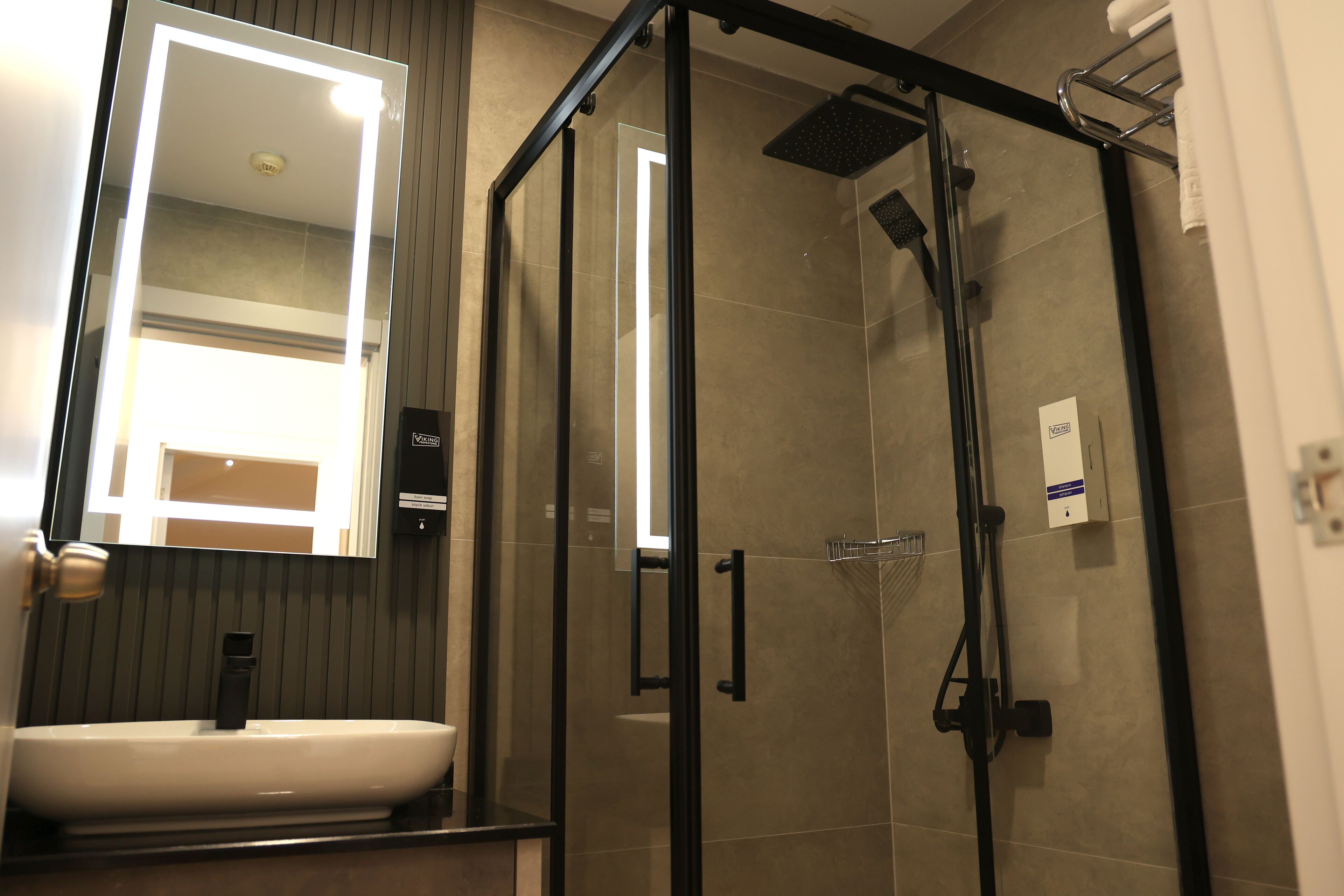 A modern bathroom with a glass-enclosed shower, a white sink, and a mirror with integrated lighting.